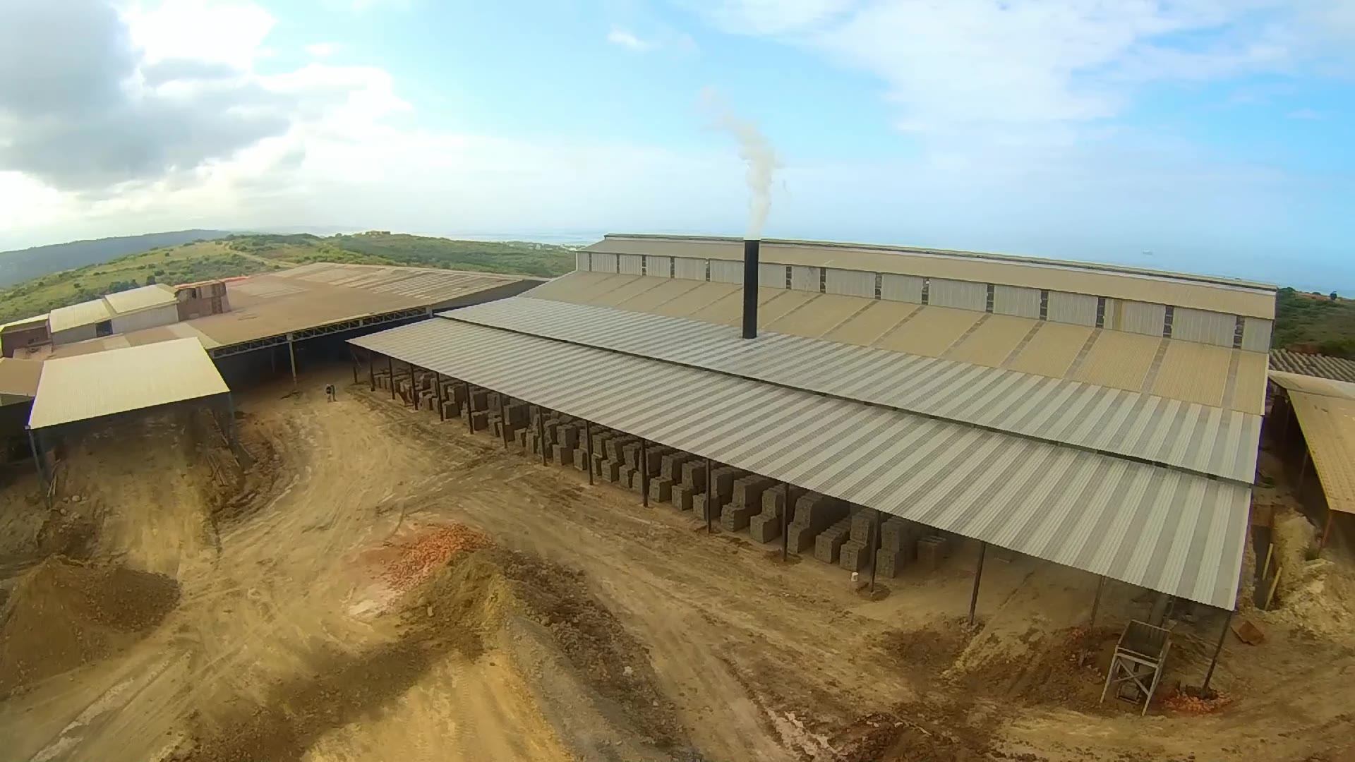 Aerial view of a brick works with long kiln and drying sheds, smoke rising from the exhaust stack